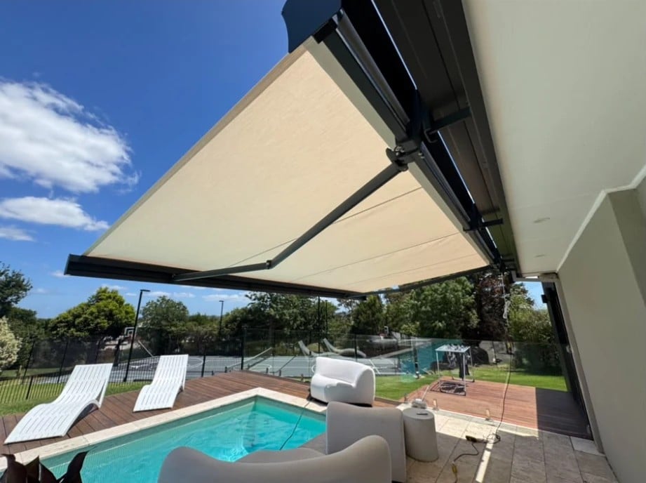 Motorised folding arm awning shading a pool deck with sun lounges